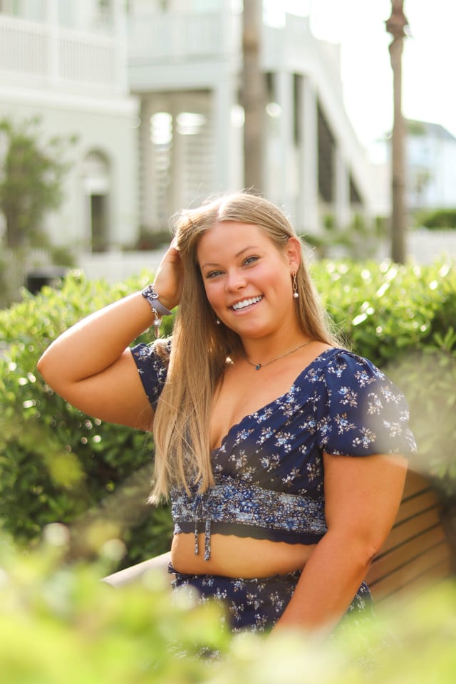 Senior in a navy floral top in front of a green hedge