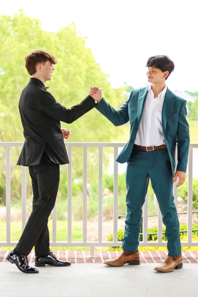 Two seniors in teal and black suits on a porch