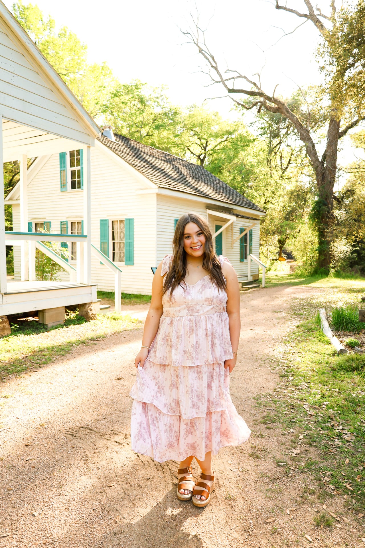 Senior in a pink floral dress in front of a farmhouse
