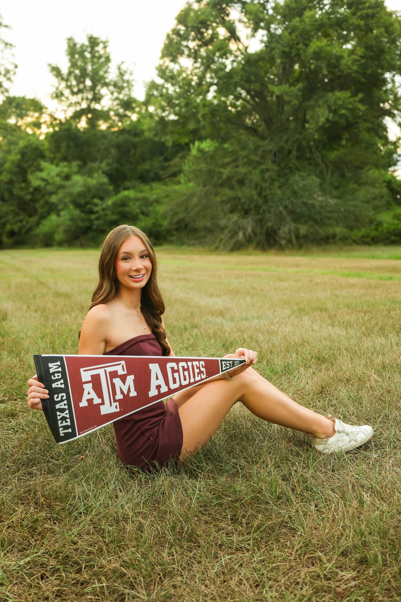 Senior in maroon dress holding a Texas A&M Aggies pennant in a field