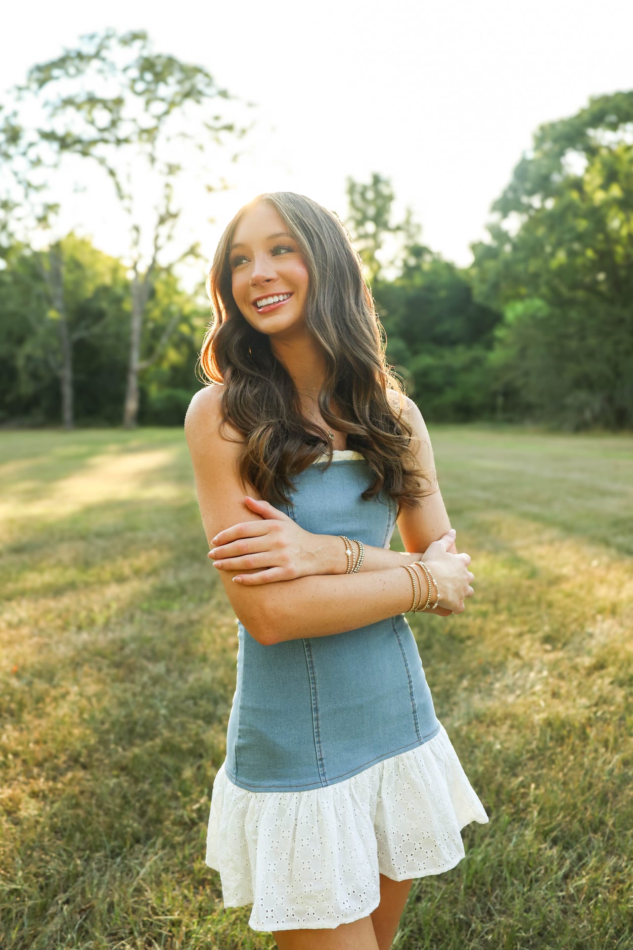 Senior in denim and eyelet dress in a sunlit field