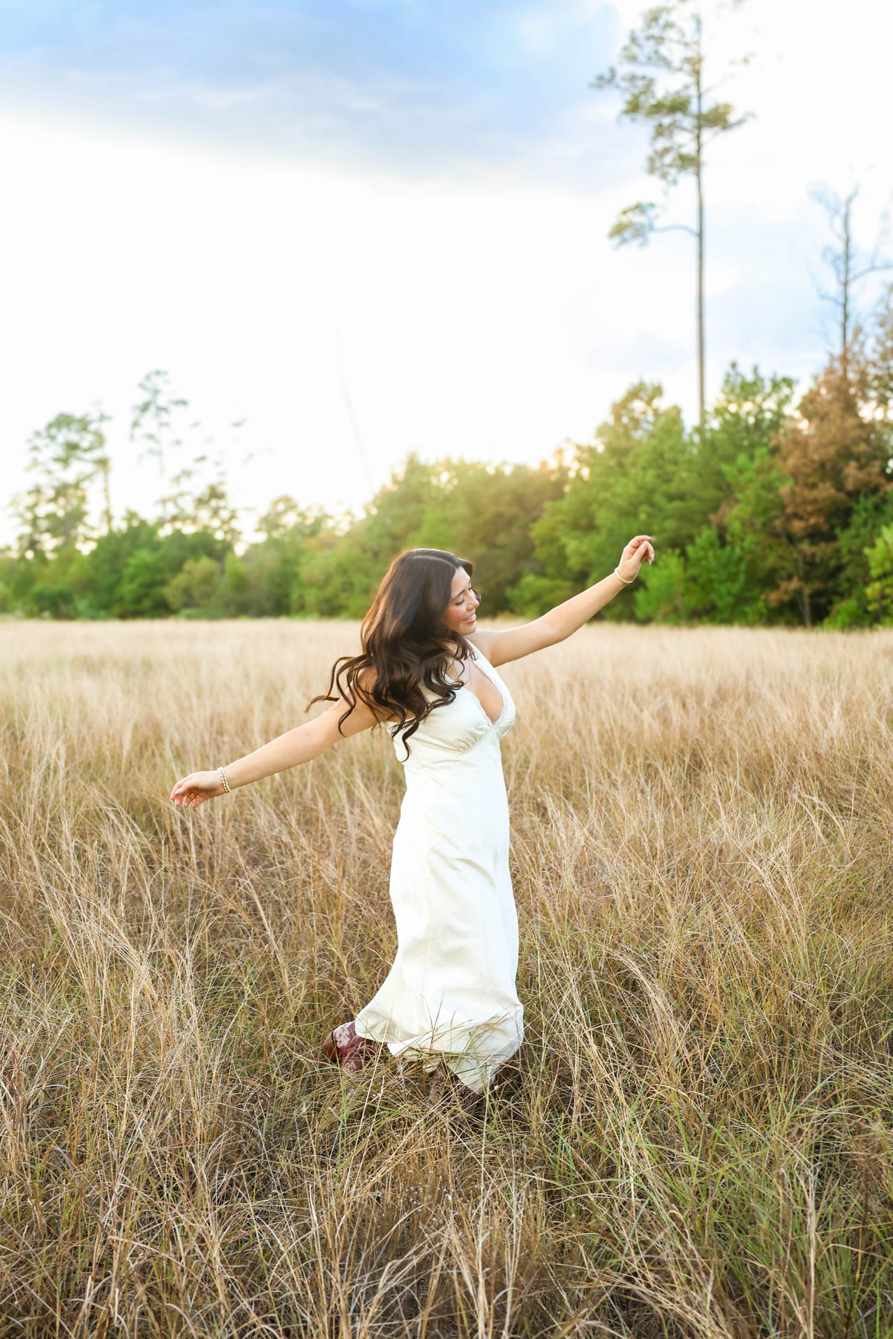 Senior in white slip dress dancing in a tall grass field at sunset