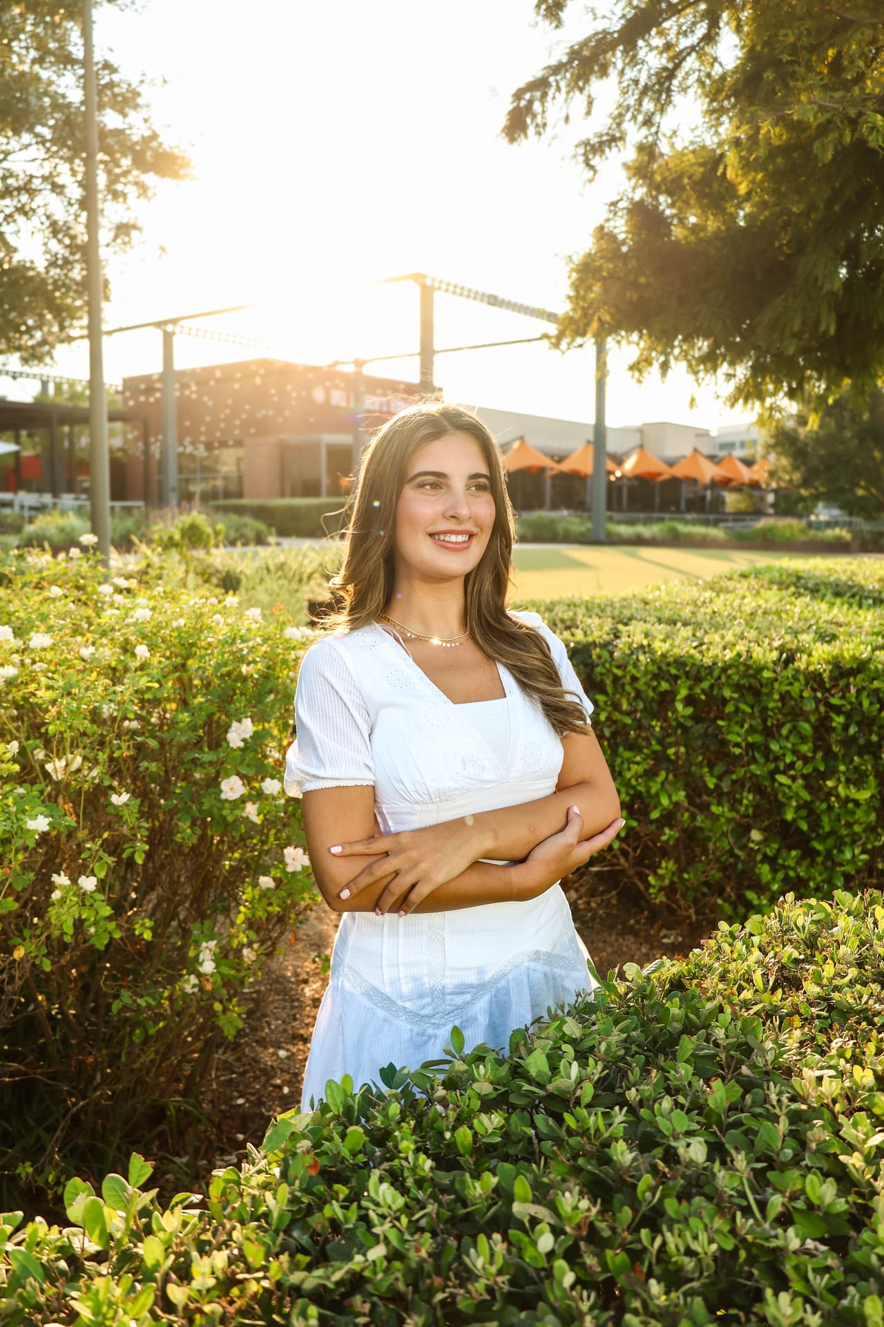 Senior in white dress with crossed arms in a sunlit garden