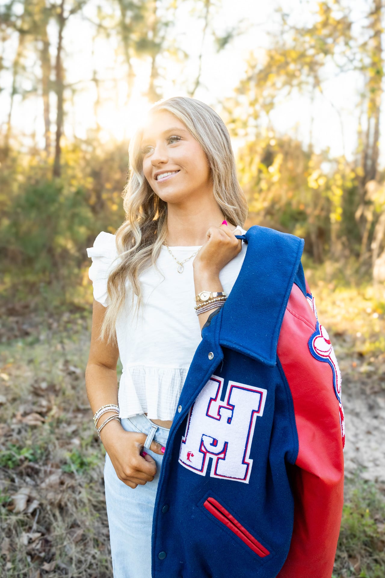 Senior holding a letterman jacket in a sunlit field
